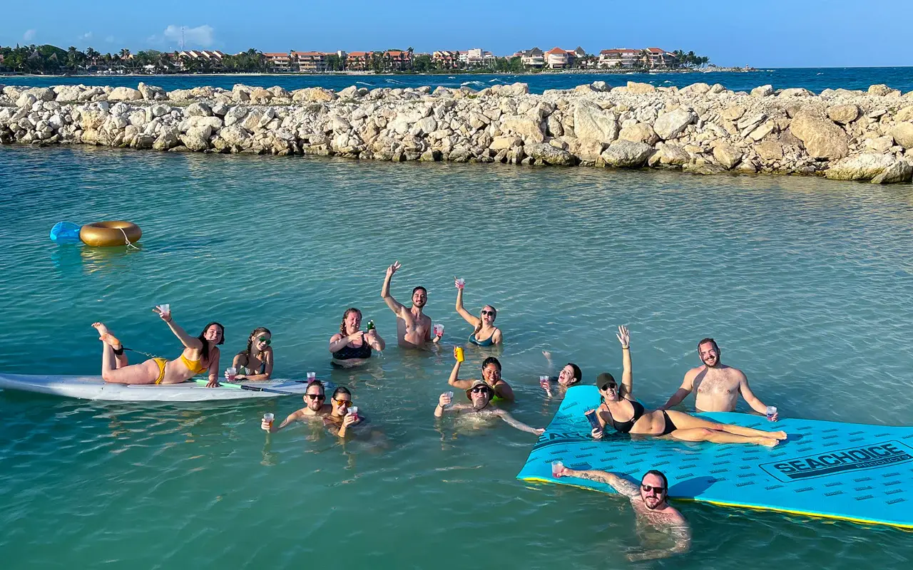 Guests lounging on a blue floating mat and paddleboard in a calm Riviera Maya lagoon by a rocky breakwater