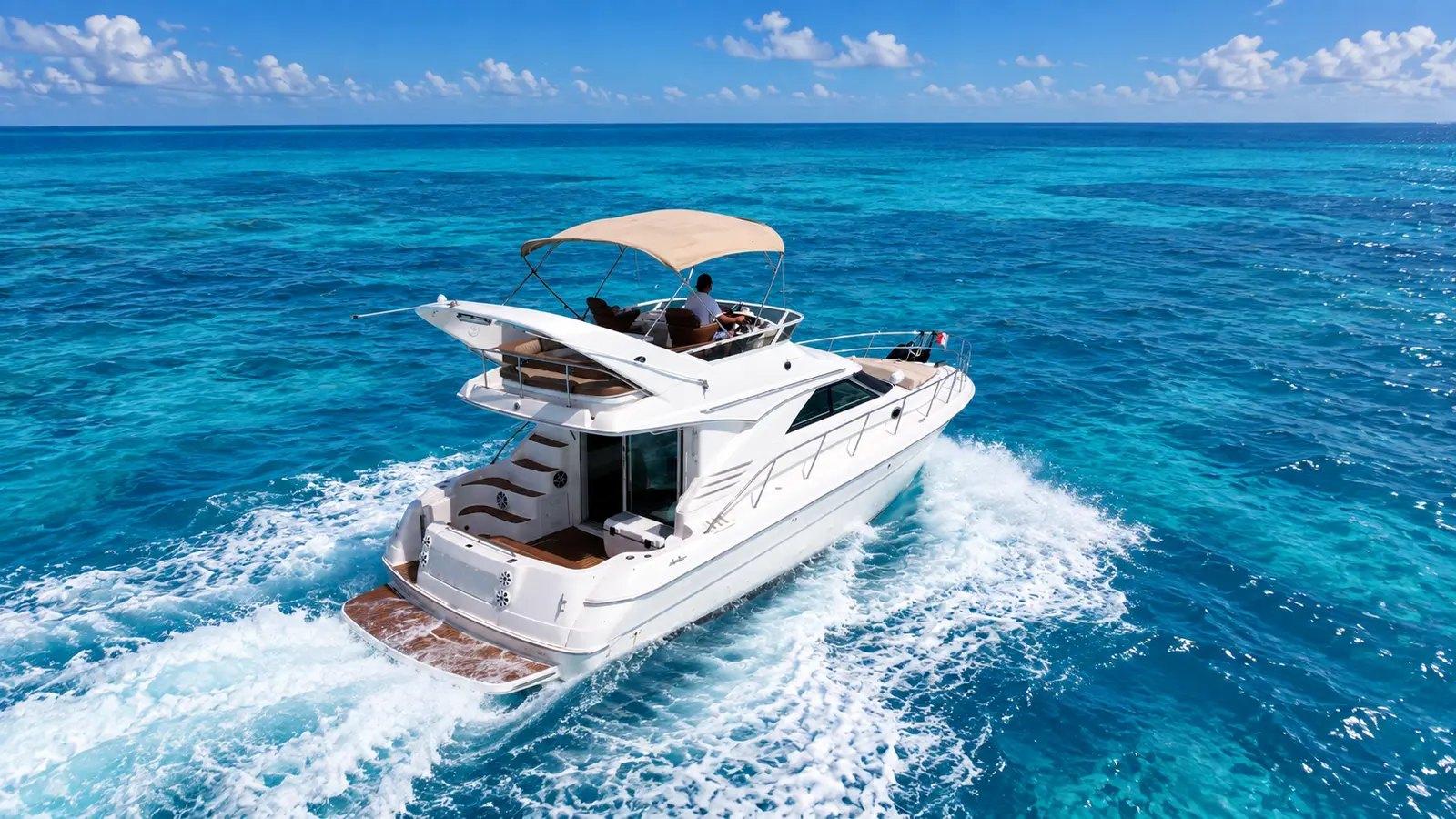 Flybridge motor yacht carving a white wake through deep blue water off Cancún