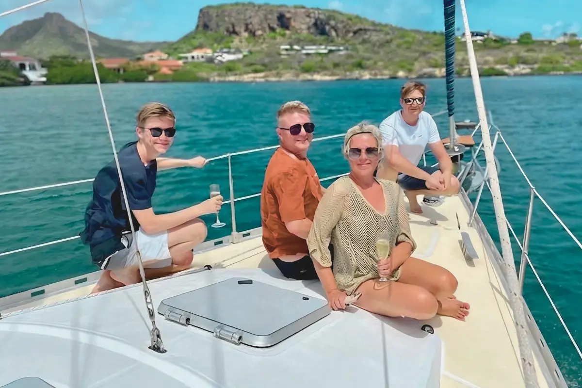 Four guests with drinks relaxing on the foredeck as the sailing yacht crosses the Spanish Waters
