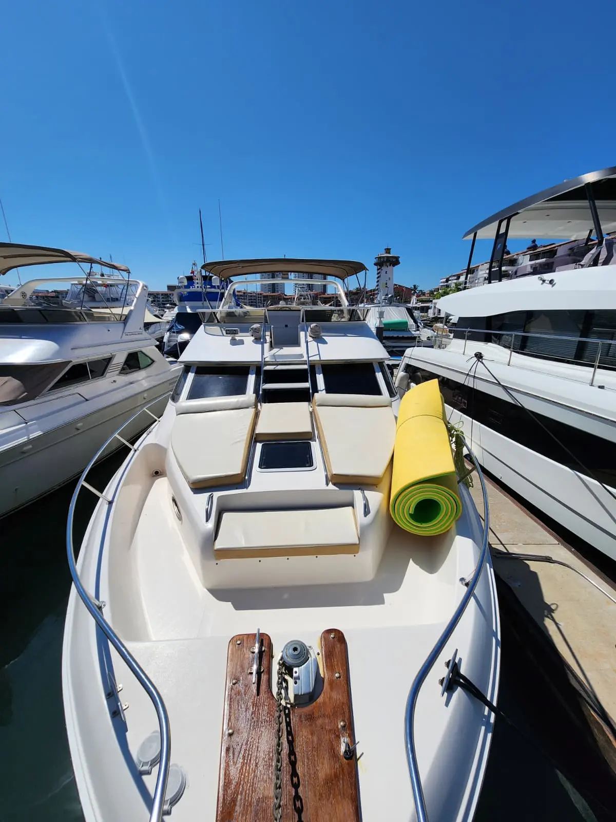 Bow deck of the yacht with sun cushions and a rolled yellow float mat, moored between boats