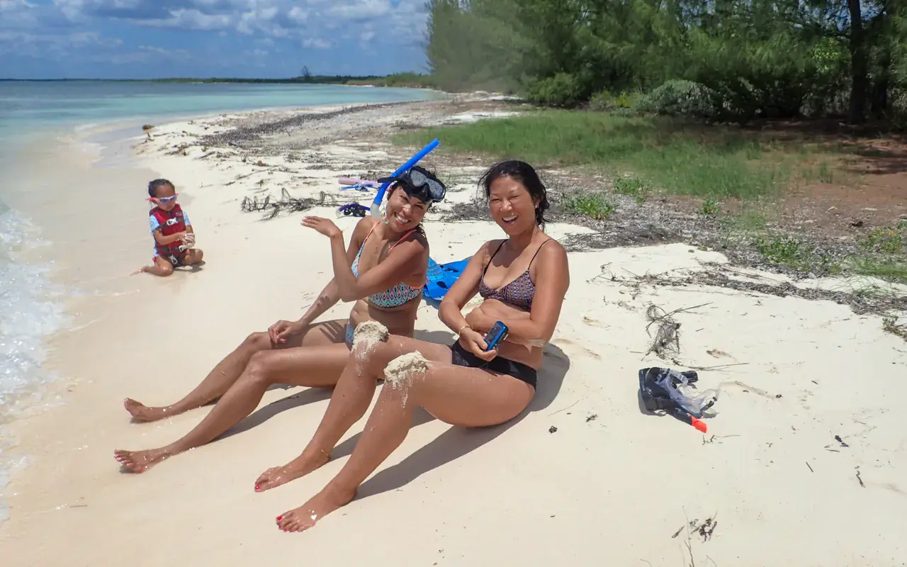Two women lounging on a quiet Riviera Maya beach with snorkel gear, a child nearby