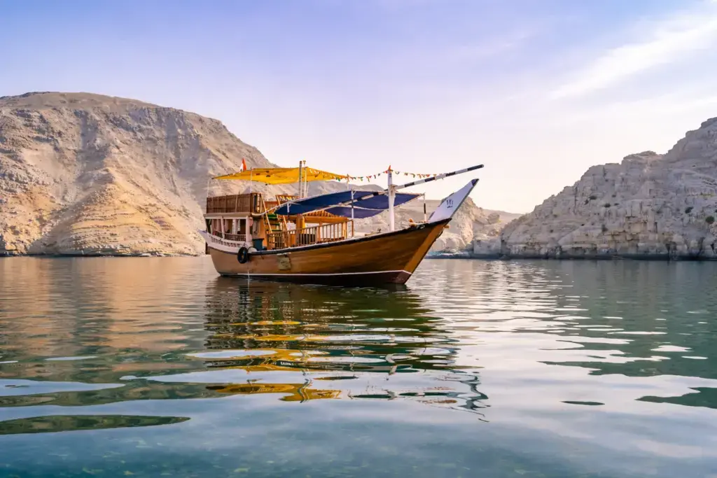 Traditional dhow cruising through the Musandam Fjords in Oman, surrounded by dramatic limestone cliffs and calm turquoise waters.