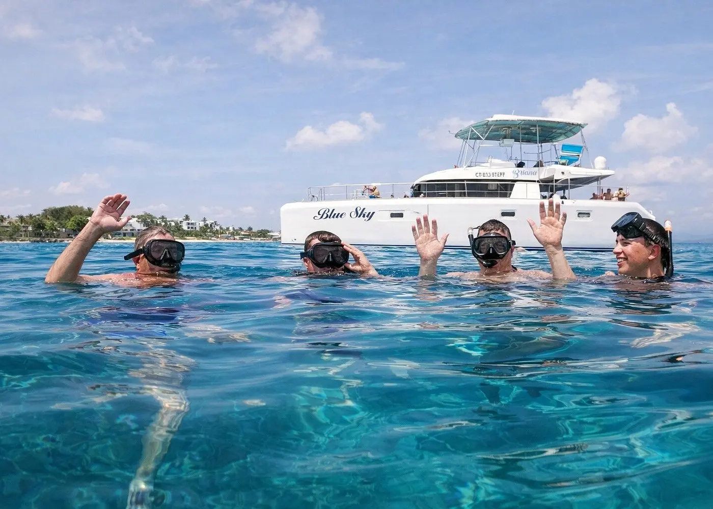 Four snorkelers in masks waving from the sea off Puerto Plata, the power catamaran behind them