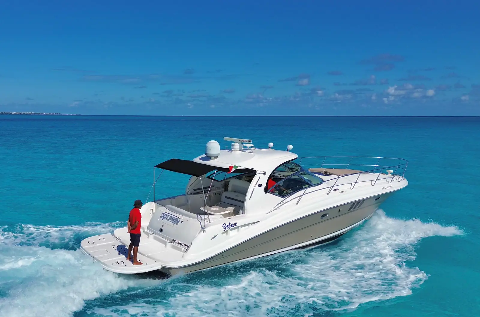 Motor yacht with a black sunshade speeding across turquoise water off Cancún, a man in red standing at the stern
