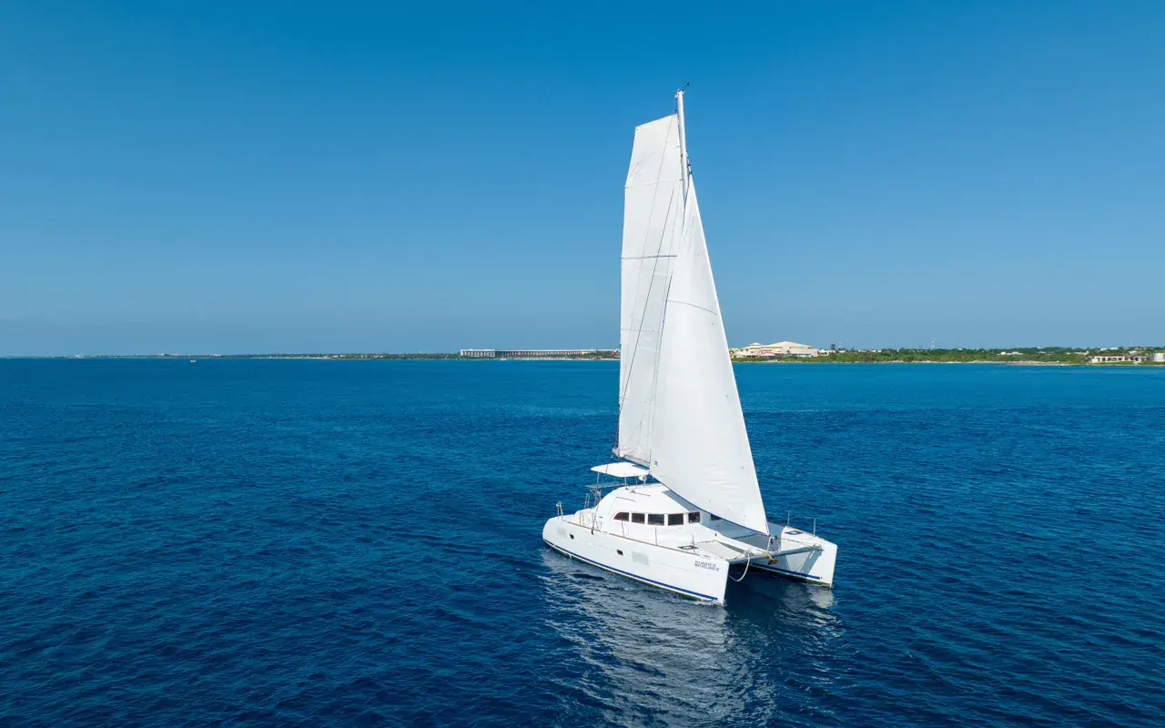 Sailing catamaran under full sail on calm blue sea along the Riviera Maya shoreline