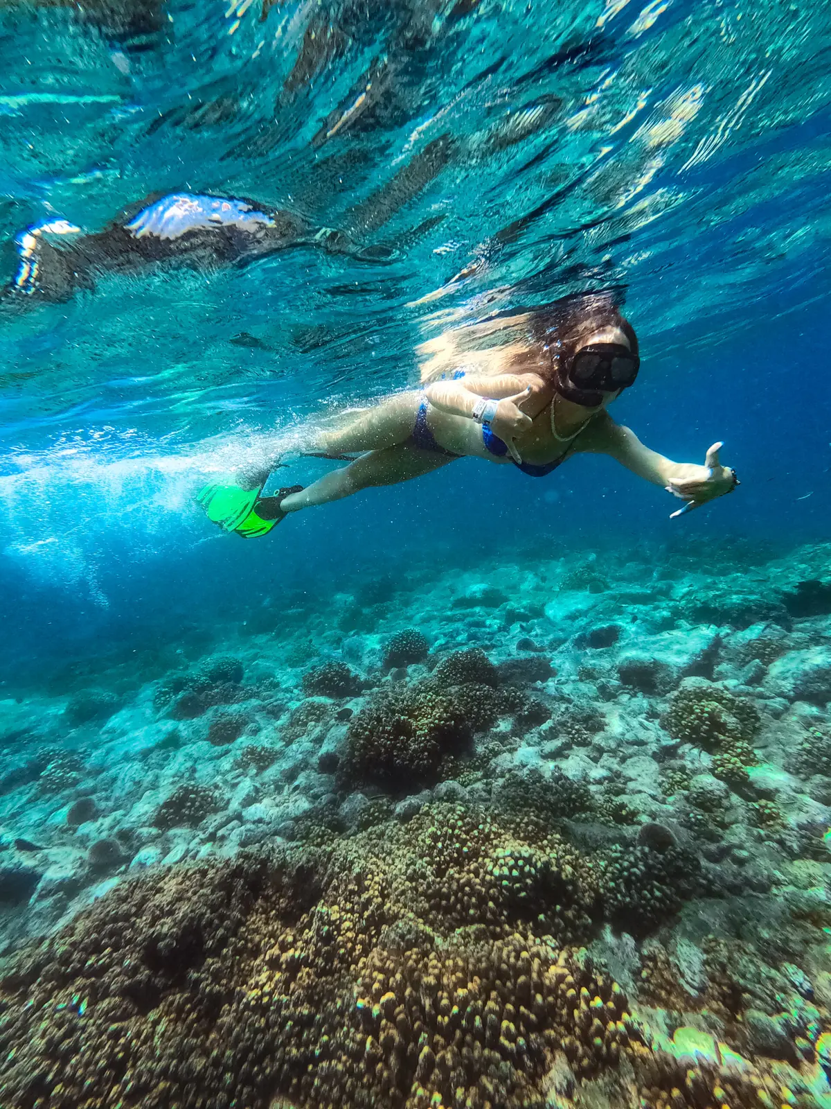 A snorkeler in a mask and fins swims over a coral reef in clear turquoise water