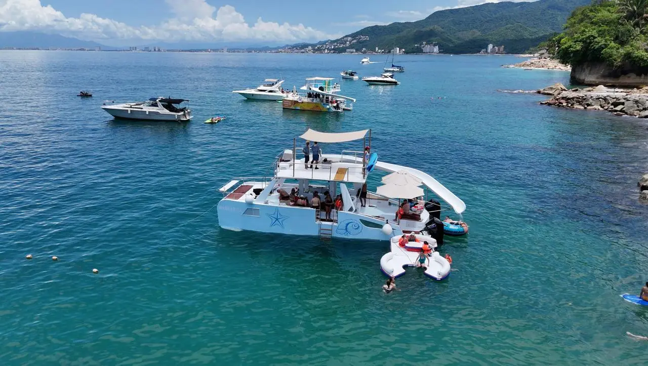 Party catamaran with a water slide anchored near the rocky shore of Banderas Bay among other boats