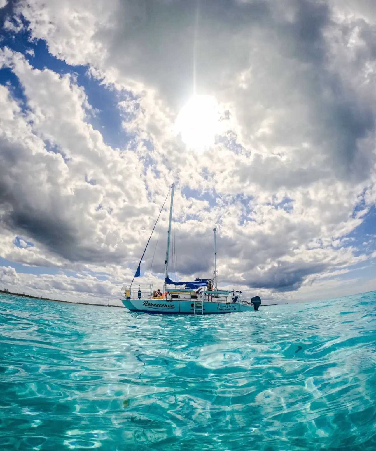 Catamaran anchored in turquoise shallows under a sunburst and puffy clouds in Cozumel