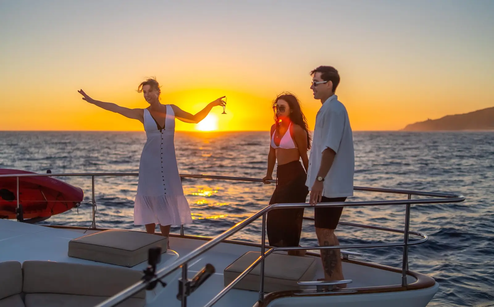 A woman in white raises her arms at the catamaran's bow as a couple watches the sunset off Puerto Vallarta