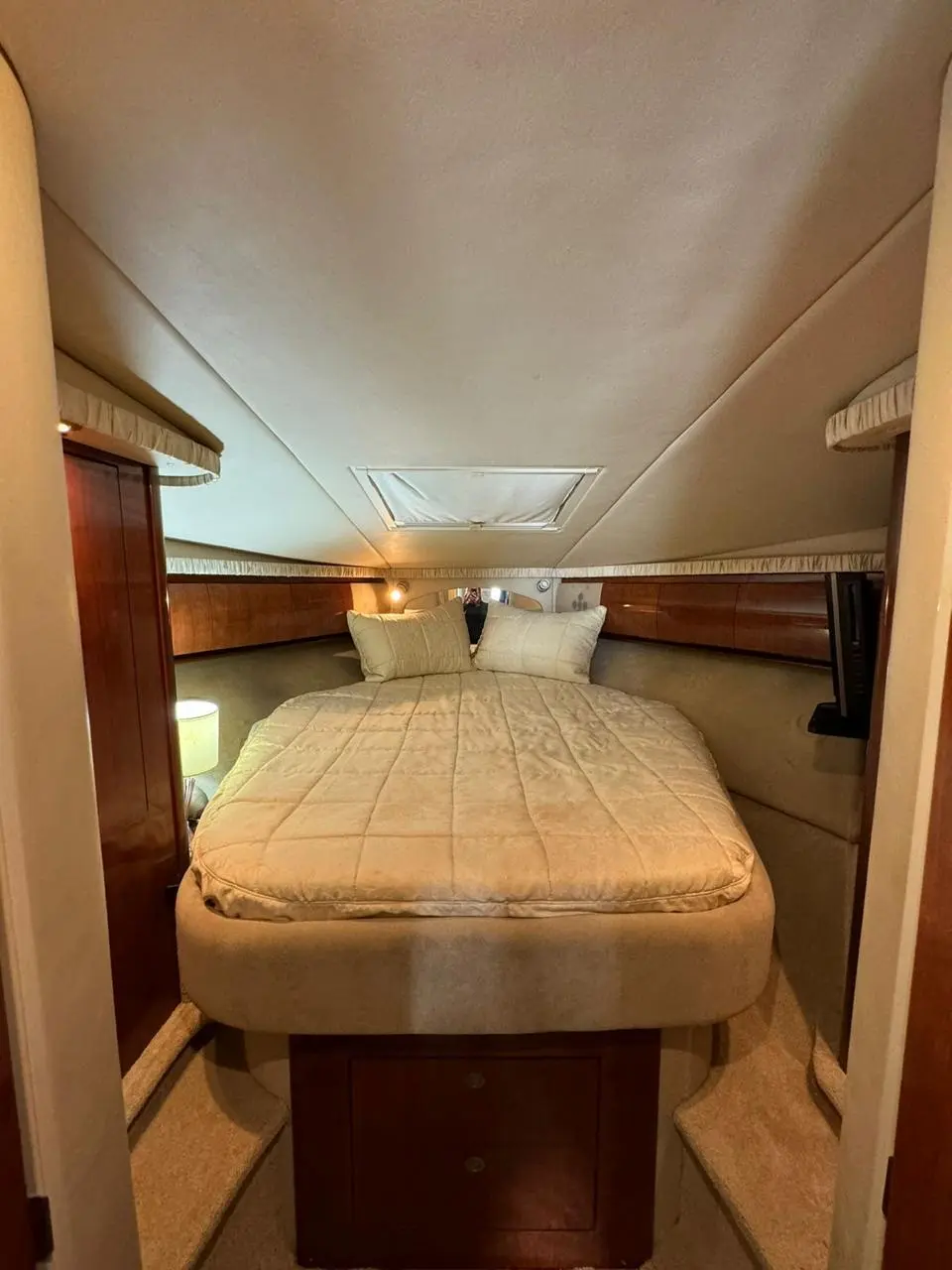 Yacht cabin with a beige-covered double bed, wood trim and an overhead hatch