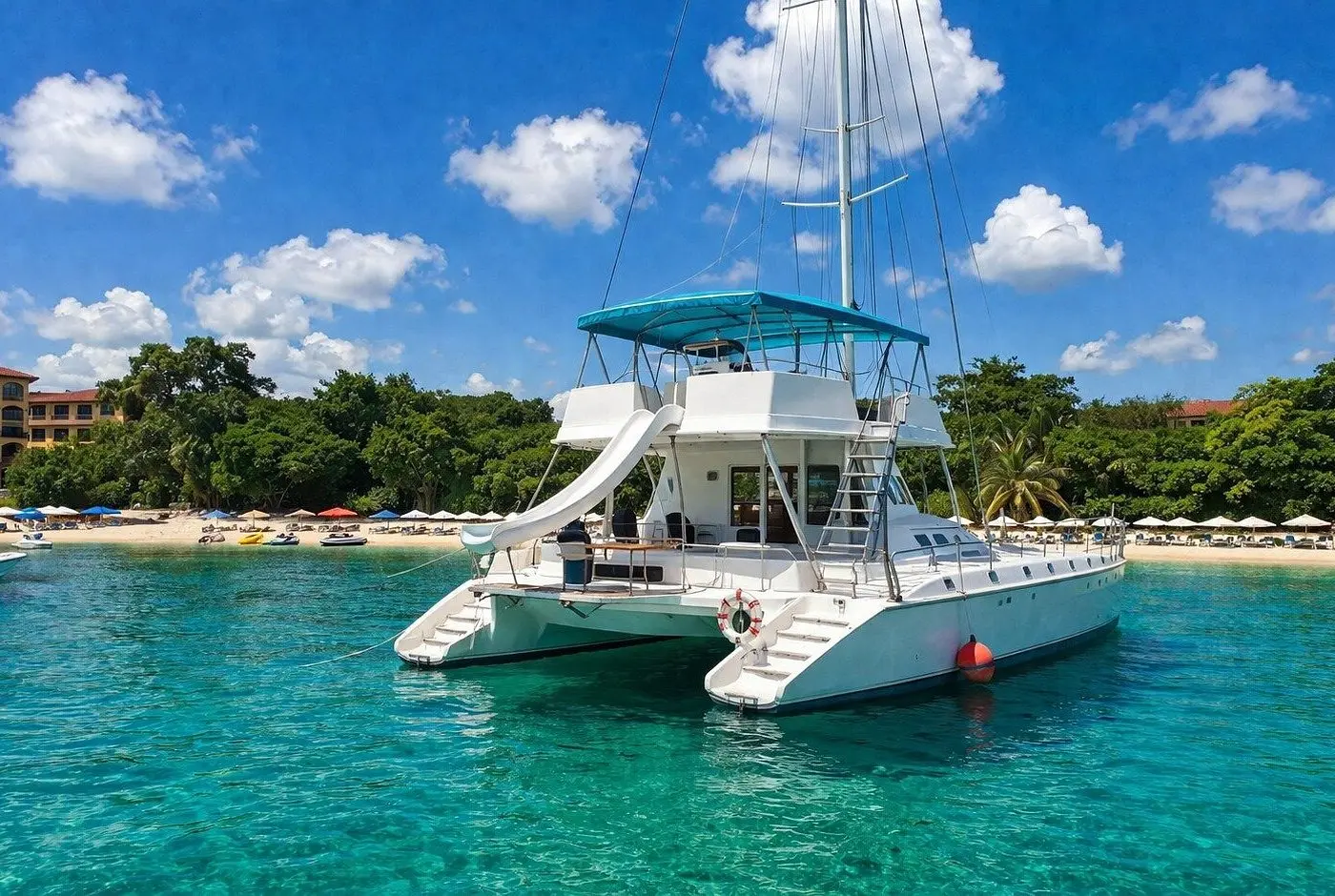 Sailing catamaran with a waterslide anchored in turquoise water off a Puerto Plata beach lined with umbrellas