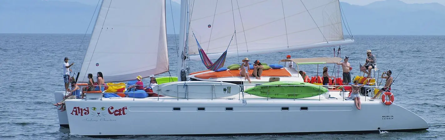 Sailing catamaran under full sail off Puerto Vallarta, guests lounging on bean bags and a hammock