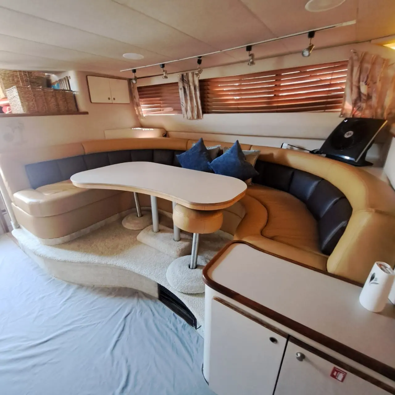 Curved leather dinette with blue cushions and a table beneath shaded windows in the yacht's cabin