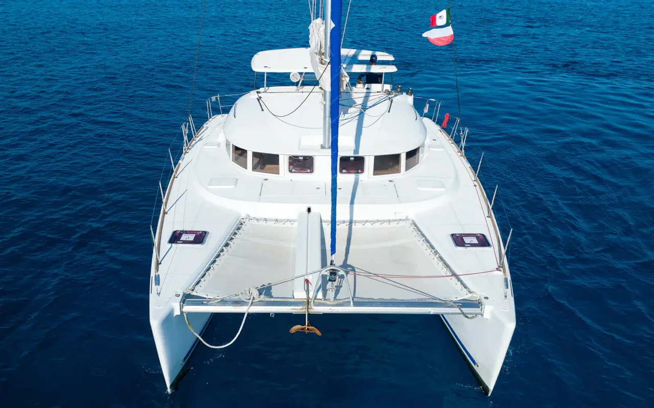 Head-on aerial view of a sailing catamaran's bow trampolines and mast on deep blue water